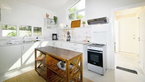 Una cocina moderna con armarios blancos, una mesa de comedor de madera, un horno empotrado y una cafetera.