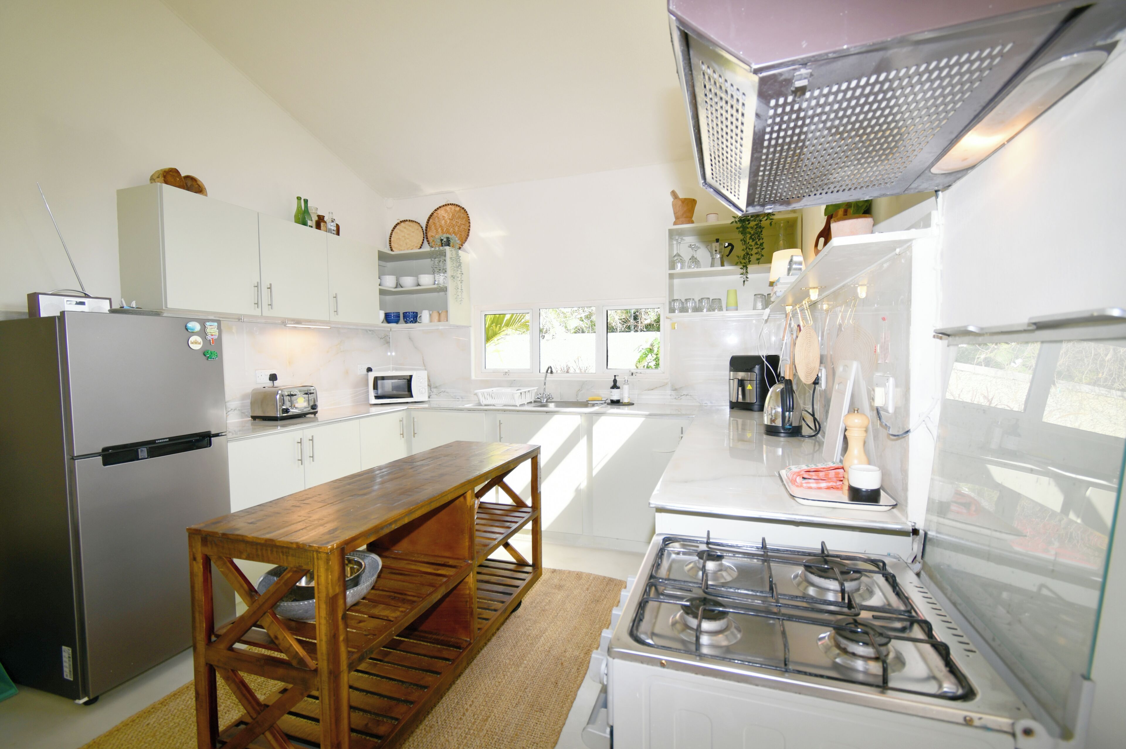 A modern kitchen with a stainless steel refrigerator, a wooden table, a gas stove, and white cabinetry.