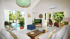 Amplia sala de estar con televisor grande, asientos cómodos y vista a una piscina y vegetación.