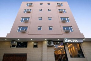 A multi-story hotel building with a flat facade, air conditioning units, and a visible entrance with a sign. - Hotel Urban Tree At Delhi Airport (New Delhi)