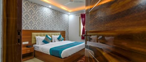 A hotel room with a wooden bed, a nightstand, a patterned wall, and a ceiling fan.