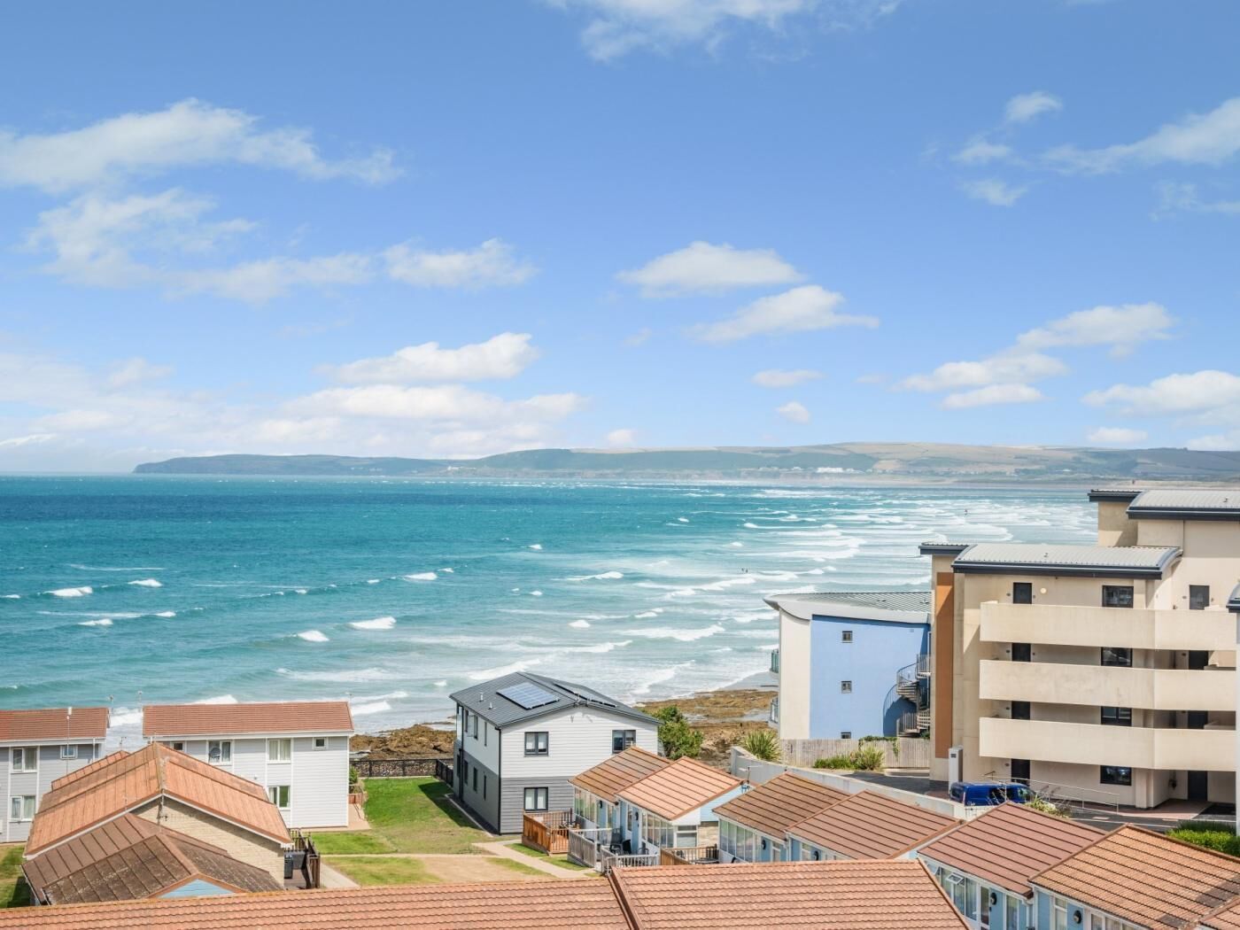 Un quartier résidentiel situé sur la côte, avec des maisons, une vue sur la mer et un ciel dégagé.