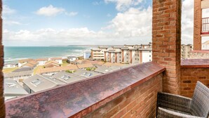 A balcony with a view of the sea and buildings, a wicker chair, and a brick wall. - 2 Bed in Bideford (oc-oce16) (Westward Ho!)