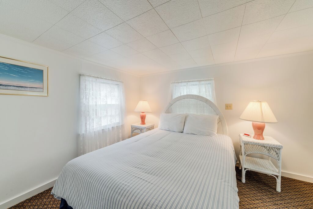A hotel room with a large bed, two bedside tables with lamps, a window with sheer curtains, and a framed picture on the wall.