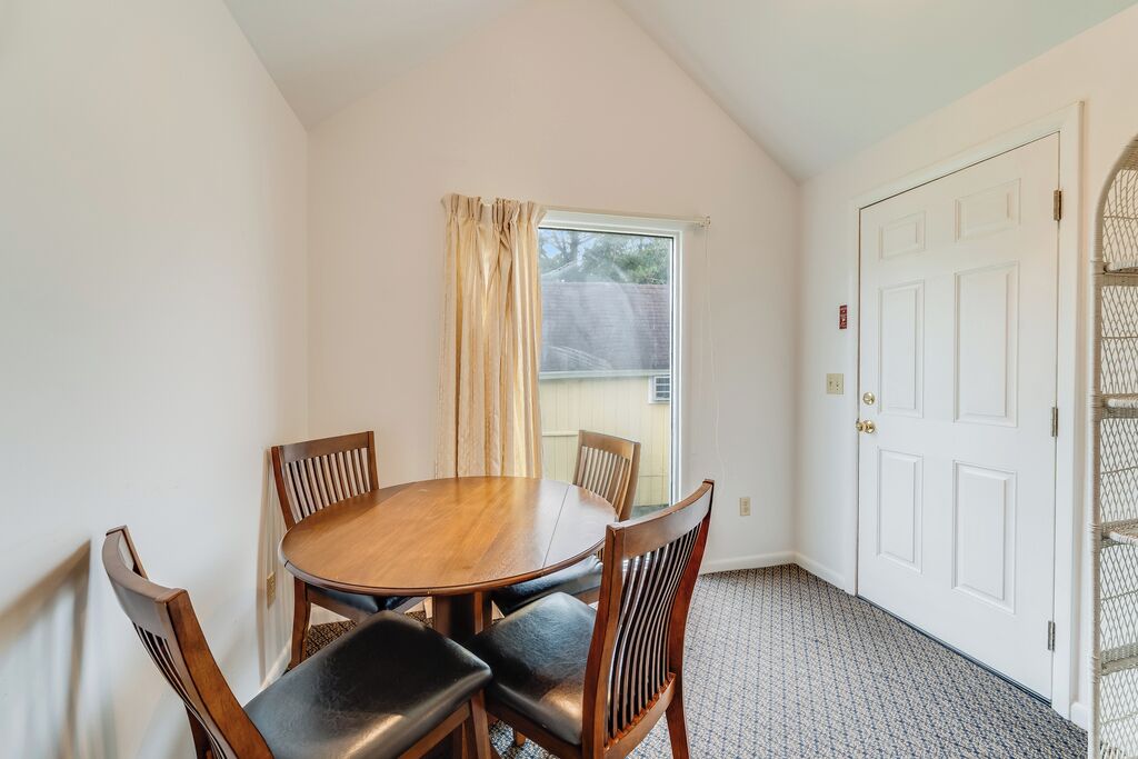 A room with a round wooden table and four chairs, a white door, and a window with curtains.