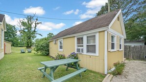 A small yellow building with a pitched roof, a picnic table, and a wooden fence in the background. - Dolly's Place 6 by Seaside Vacations! (Chincoteague Island)