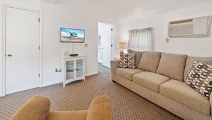 A living room with a sofa, a television, a cabinet, and a ceiling fan. - Dolly's Place 6 by Seaside Vacations! (Chincoteague Island)
