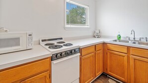A kitchen with a microwave, stove, and sink, wooden cabinets, and a window with blinds. - Dolly's Place 6 by Seaside Vacations! (Chincoteague Island)