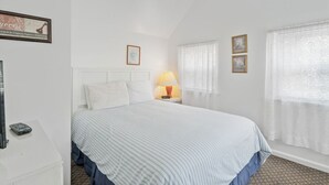 A bedroom with a bed, a nightstand, a lamp, and a framed picture on the wall. - Dolly's Place 6 by Seaside Vacations! (Chincoteague Island)