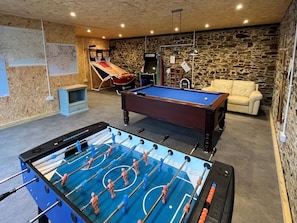 Ein Raum mit einem Kicker, einem Billardtisch, einer Couch und einer Steinwand.