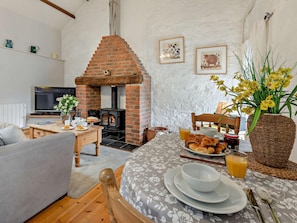 Ein gemütliches Wohnzimmer mit Kamin, einem für das Frühstück gedeckten Esstisch und einem Fernseher.