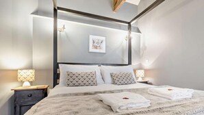 Ein ordentlich bezogenes Bett mit einer gemusterten Decke, zwei Kissen und einem gefalteten Handtuch auf einem strukturierten Teppich.