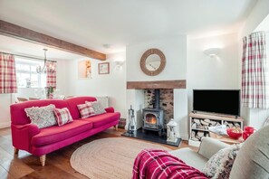 A living room with a red sofa, a fireplace, a TV, and a dining area with plaid curtains. - 3 Bed in Bridport (oc-dc055) (Burton Bradstock)