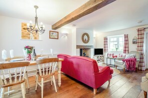A dining area with a wooden table and chairs, a red sofa, a fireplace, and a television. - 3 Bed in Bridport (oc-dc055) (Burton Bradstock)