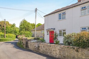 A white building with a red door, a stone wall, and a road. - 3 Bed in Bridport (oc-dc055) (Burton Bradstock)