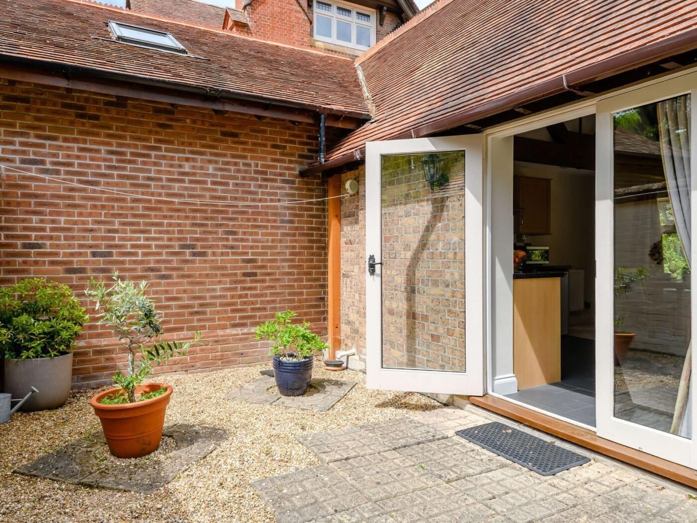Une maison en briques avec un patio, une porte-fenêtre coulissante donnant sur la cuisine et des plantes en pot.