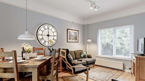 A dining area with a wooden table, chairs, a large wall clock, and a sofa. - 2 Bed in Newton Abbot (oc-primc) (Hennock)