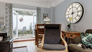 A living room with a wooden chair, a sofa, a large wall clock, and a view through a glass door. - 2 Bed in Newton Abbot (oc-primc) (Hennock)
