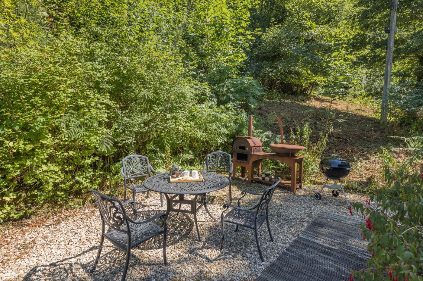 A patio with a round table and chairs, surrounded by dense greenery.