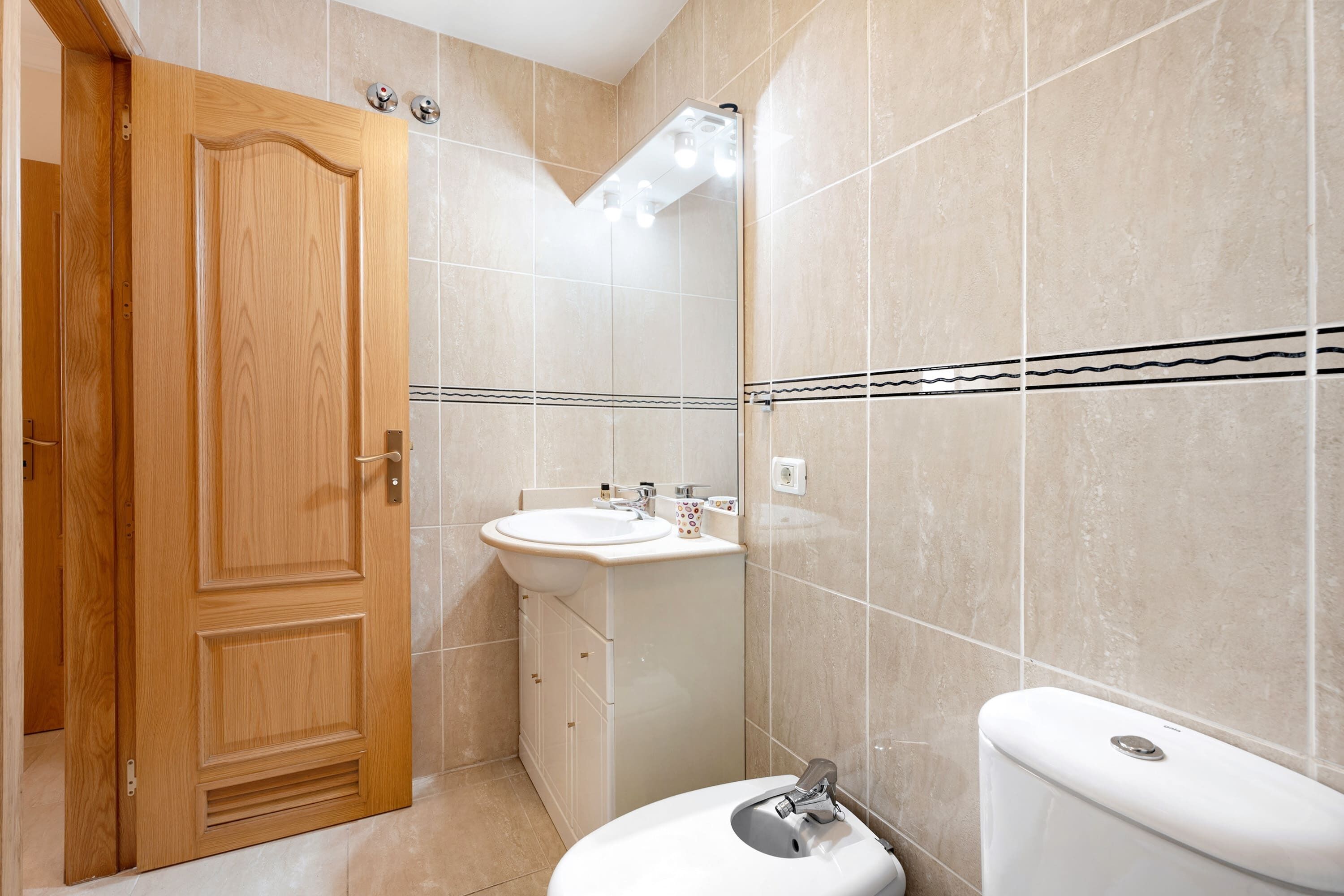 A bathroom with a wooden door, a sink, a toilet, and tiled walls.