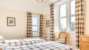 Ein Schlafzimmer mit zwei Betten, einem Holzstuhl, einer Kommode und einem Fenster mit Vorhängen.