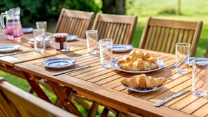 Ein Holztisch draußen gedeckt mit Tellern, Gläsern und einer Kanne.
