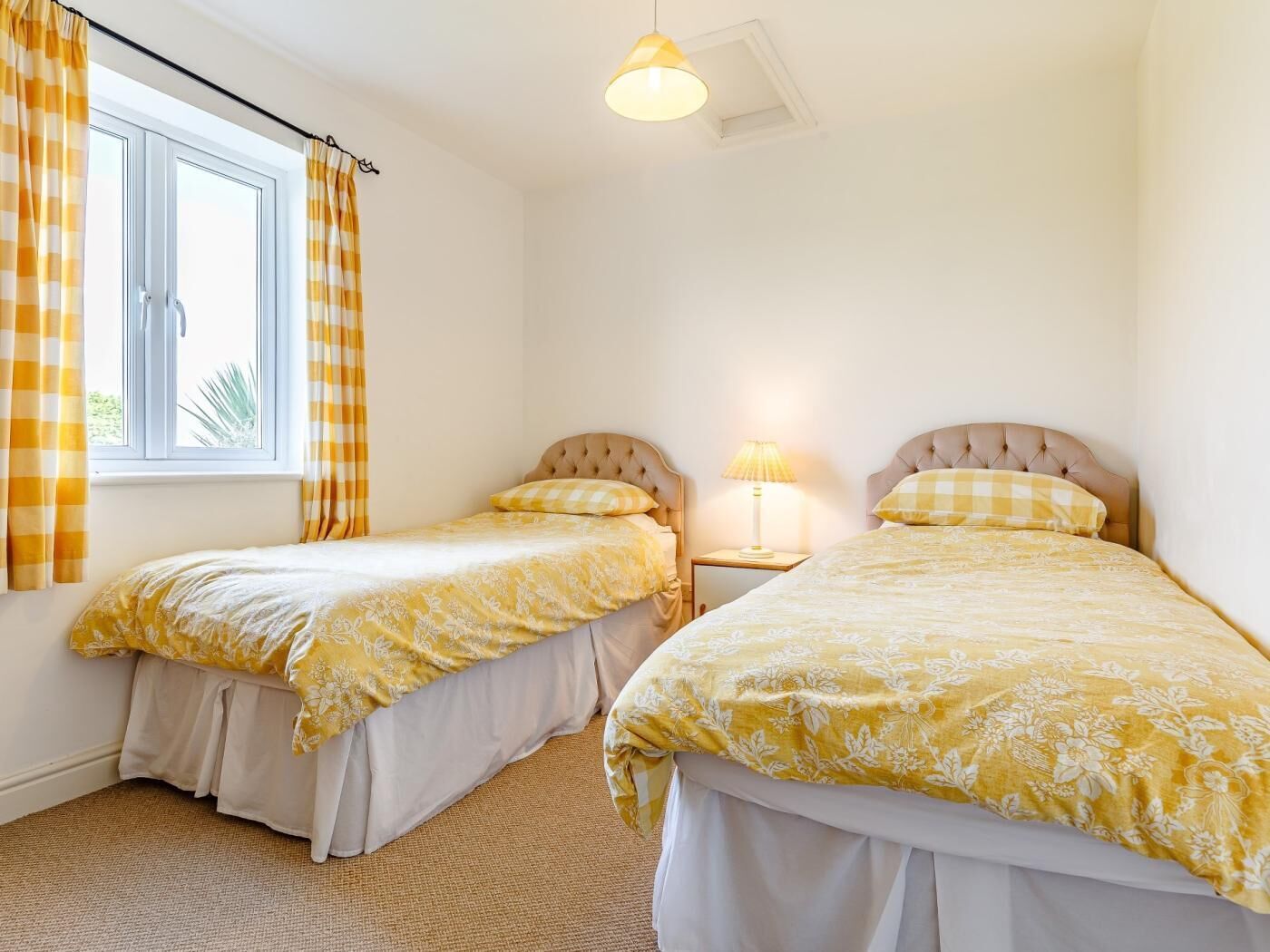 Een slaapkamer met twee bedden, een raam met gordijnen, een plafondlamp en een nachtkastje met een lamp.
