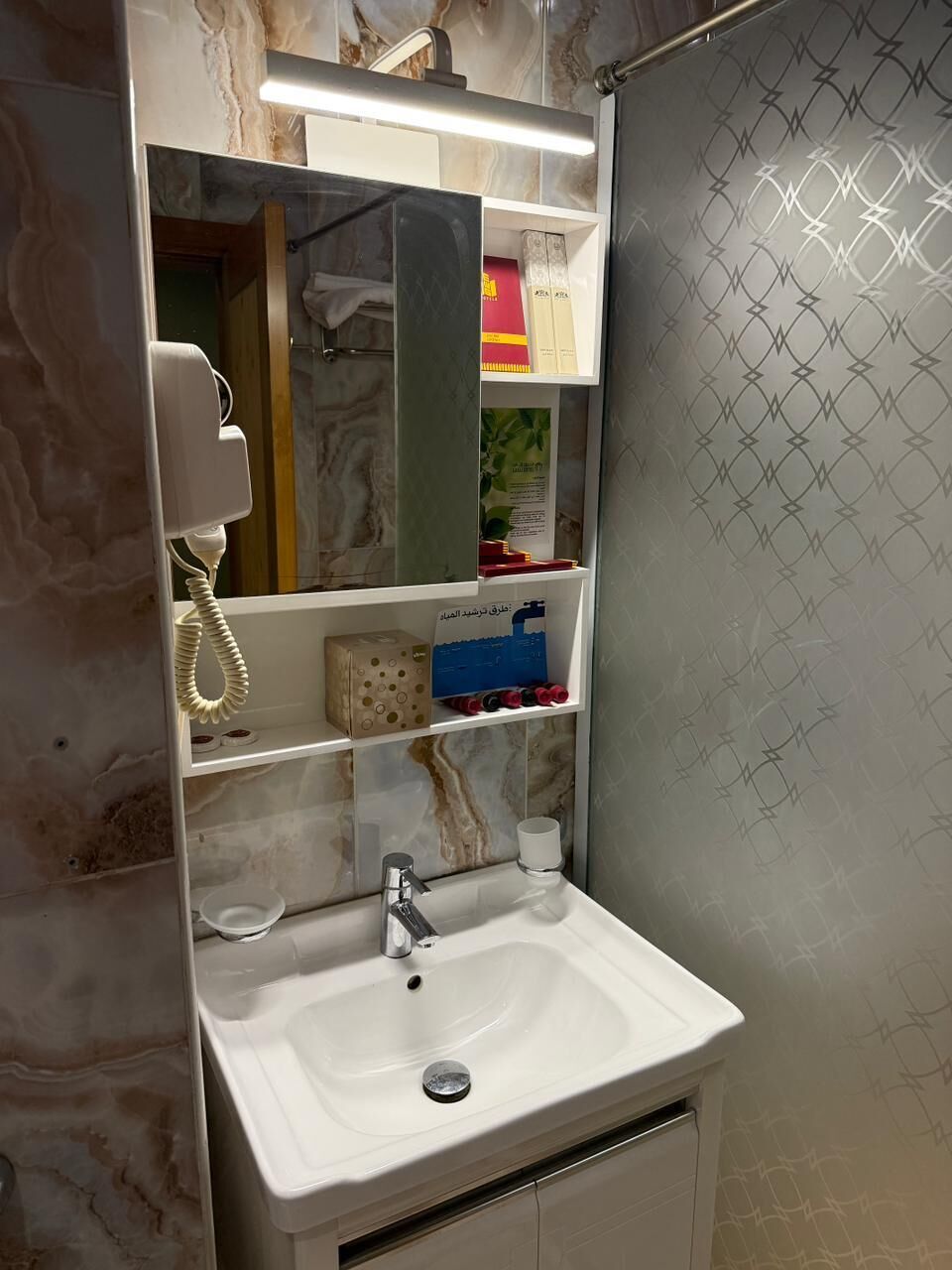A bathroom with a marble sink, a mirror, shelves with toiletries, and a shower curtain with a geometric pattern.