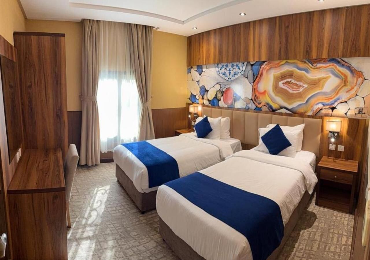 Una habitació d'hotel amb dos llits, una taula, una cadira, un quadre abstracte gran a la paret i un armari de fusta.