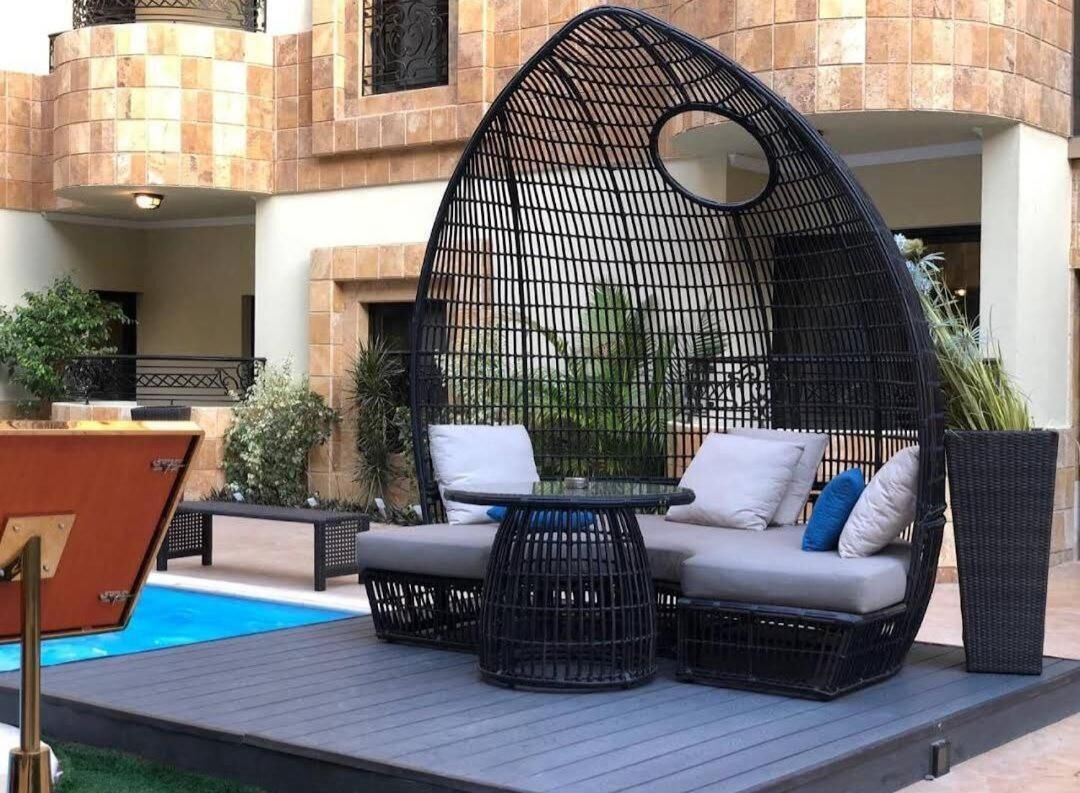 A poolside seating area with a round table and cushions, surrounded by a black mesh structure.