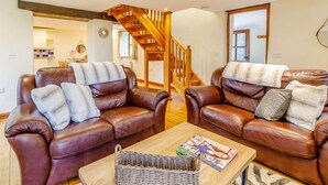 A living room with two leather sofas, a wooden staircase, and a kitchen in the background. - 2 Bed in Holsworthy (oc-gmead) (Holsworthy Hamlets)