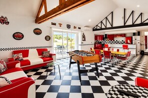 Ein Zimmer mit Schachbrettmuster-Boden, einem Kicker, einem rot-weißen Sofa und einer Küche mit roten Schränken.