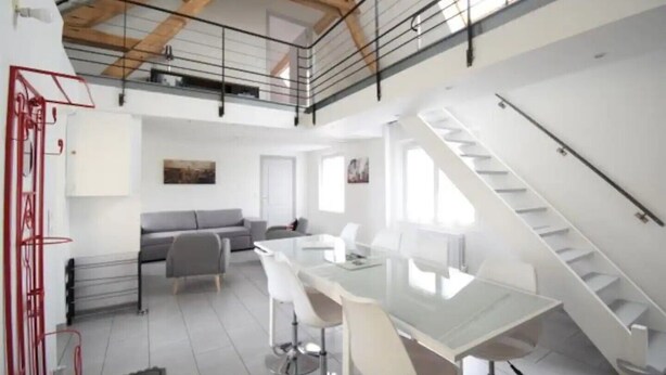 A spacious loft apartment with a high ceiling, a dining area, a living room, and a staircase. - Two charming vacation rentals in a beautiful setting, accommodating up to 12 people (Clévilliers)