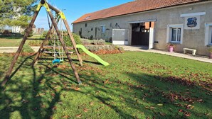 A building with a red-tiled roof, a swing set, and a paved driveway. - Two charming vacation rentals in a beautiful setting, accommodating up to 12 people (Clévilliers)
