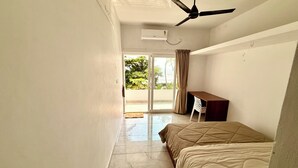 Un dormitorio con cama, ventilador de techo, escritorio y vistas a un área exterior por una puerta corrediza.