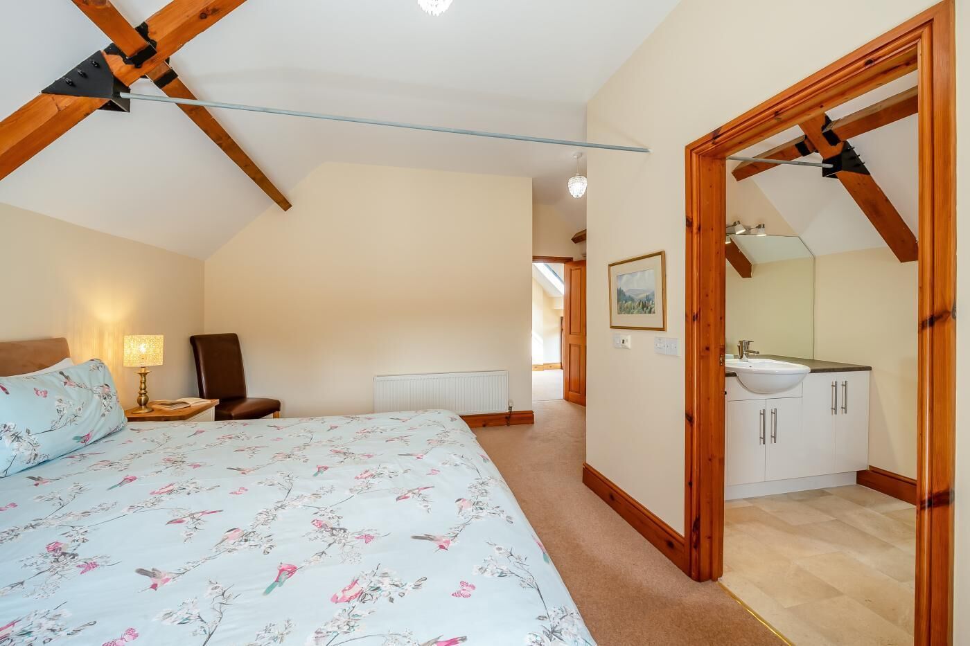 Quarto com cama, mesa de cabeceira, abajur e vista para o banheiro.