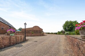 A gravel driveway leading to a wooden barn, surrounded by brick walls and potted flowers. - 4 Bed in Watchet (oc-huisb) (Beggearn Huish)