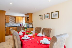 A dining area with a red tablecloth, white plates, and glasses, and a kitchen in the background.