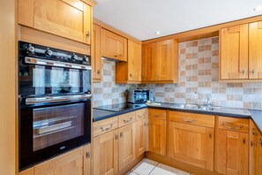 A kitchen with wooden cabinets, a built-in oven, a microwave, and a stainless steel sink. - 4 Bed in Watchet (oc-huisb) (Beggearn Huish)
