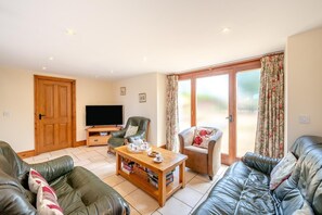 A living room with a television, leather sofas, a coffee table, and a sliding glass door leading to an outdoor area. - 4 Bed in Watchet (oc-huisb) (Beggearn Huish)