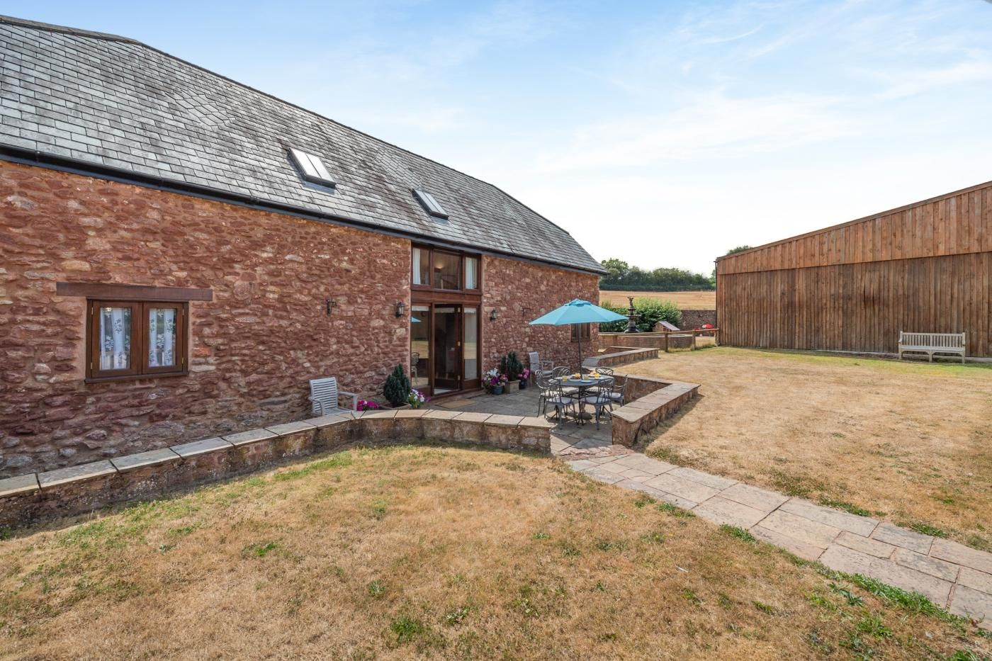 A stone building with a patio area, outdoor seating, and a wooden barn in the background.
