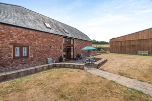 A stone building with a patio area, outdoor seating, and a wooden barn in the background. - 4 Bed in Watchet (oc-huisb) (Beggearn Huish)