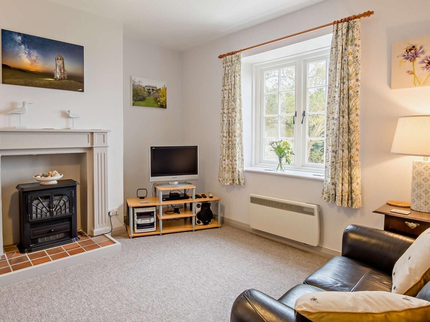 A living room with a fireplace, television, and a window with curtains.