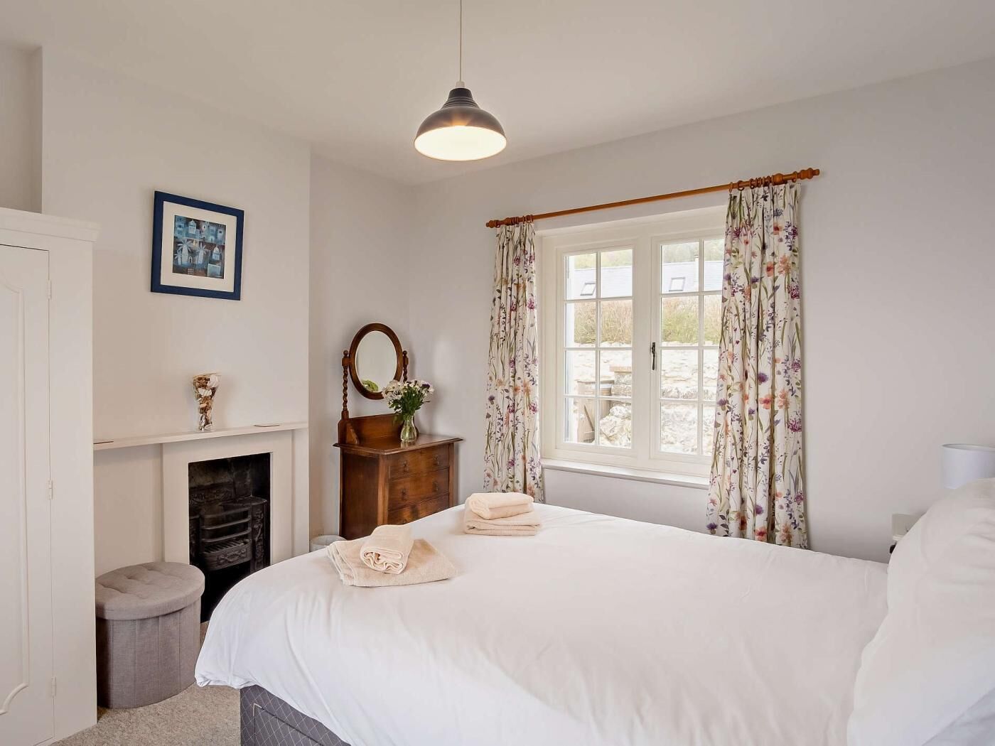 A bedroom with a bed, a fireplace, a mirror, a window with curtains, and a hanging light fixture.
