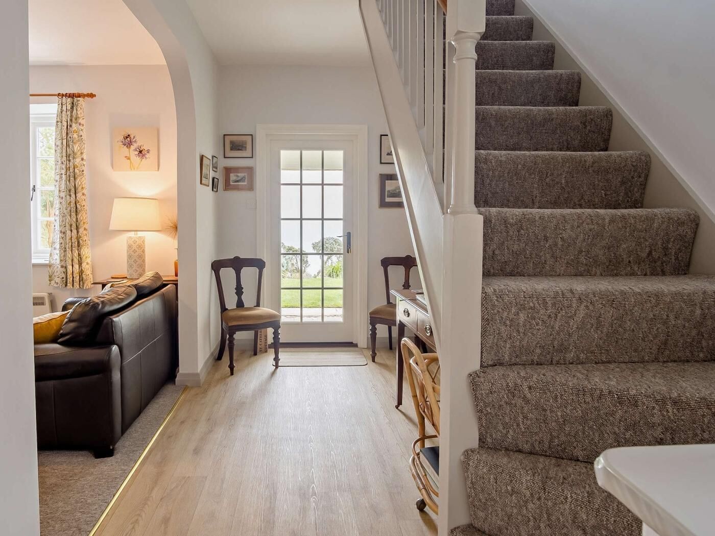 Eine Treppe führt zu einer zweiten Etage, mit Holzboden, einem dunklen Ledersofa, einem Holzstuhl und einer Lampe.