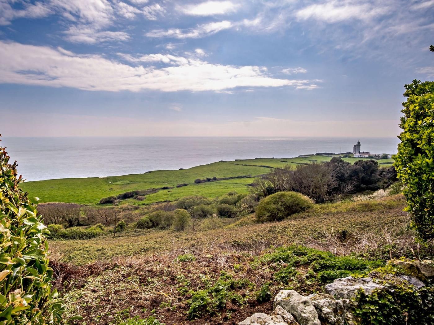 A coastal landscape with a lighthouse, rolling green hills, and a clear sky.