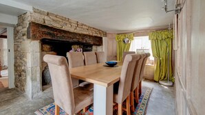 Ein Esszimmer mit Kamin aus Stein, einem Holztisch und passenden Stühlen.