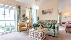 Ein Wohnzimmer mit Sofa, Sessel, Hocker und einer Deckenleuchte.