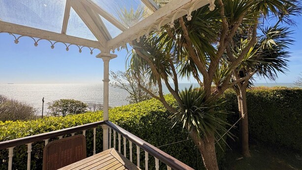 Ein überdachter Außenbereich mit Holzterrasse, weißer Geländer und Blick auf das Meer.