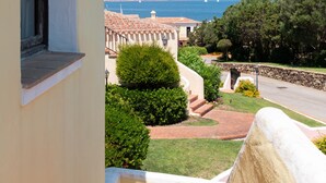 Un balcon offrant une vue sur une zone côtière, comprenant une route, de la végétation et un voilier au loin.